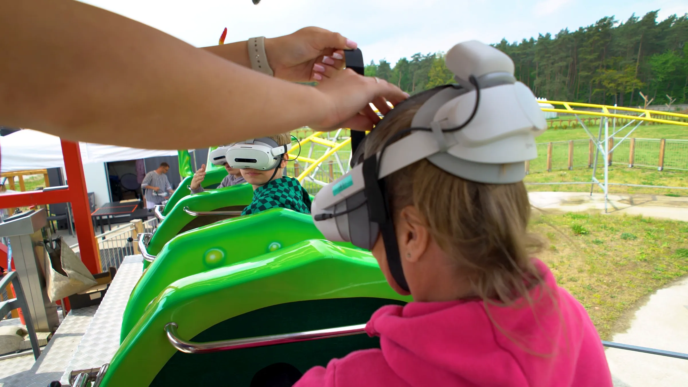 A park staff member fastens a VR headset on a seated guest before the ride