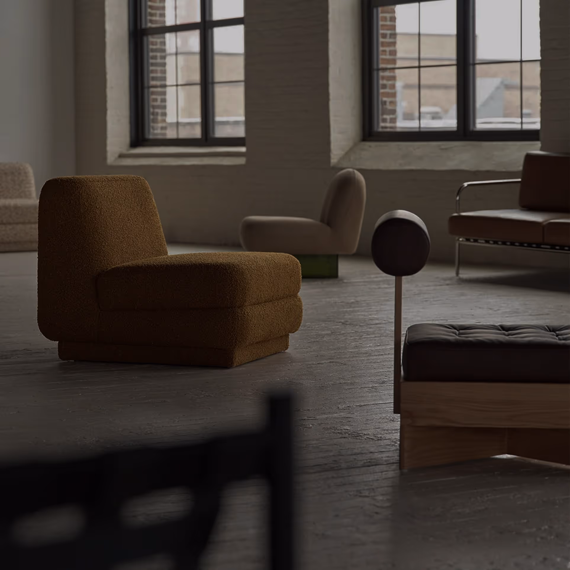 Modern living room with various upholstered chairs and a leather bench set against large windows with brick walls.