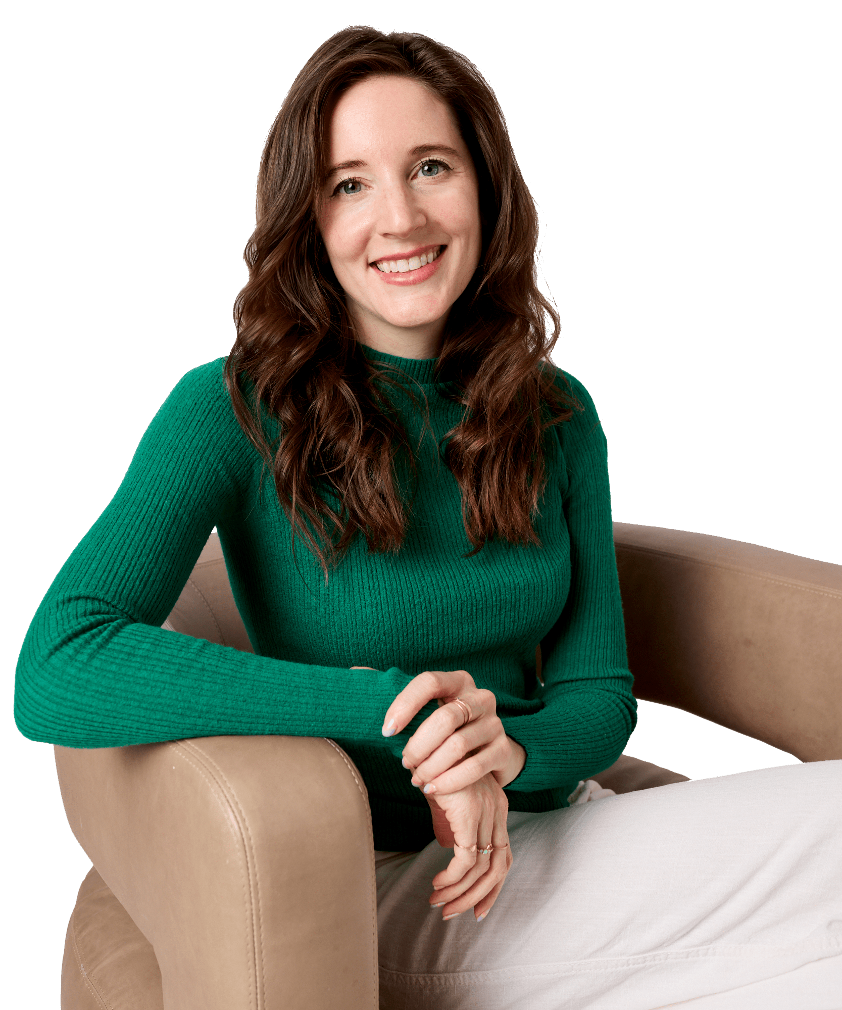 Smiling woman with long brown hair wearing a green sweater sitting on a beige chair.