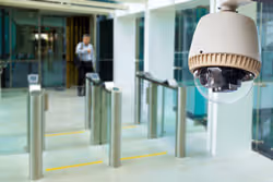 Security camera monitoring entrance with glass turnstiles and a person walking in a modern building.