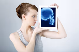 Woman holding a tablet displaying a human skull x-ray image.