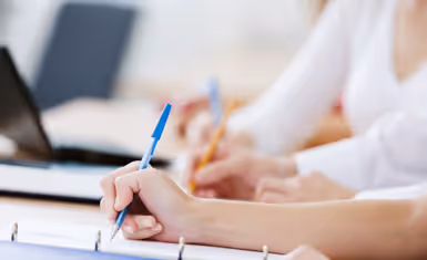 Close-up of hands writing with pens on paper in a notebook during a meeting or study session.