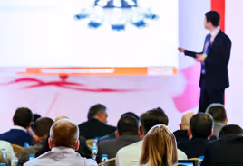 Audience seated and listening to a blurred speaker presenting at a conference or seminar.