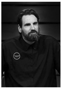 Black and white portrait of a man with a beard and mustache wearing a dark shirt with a circular logo on the chest.