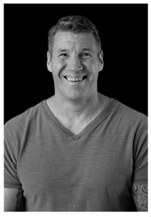 Smiling middle-aged man wearing a V-neck T-shirt against a black background.