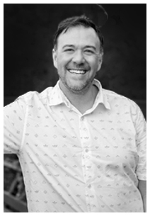 Smiling man with short hair and beard wearing a patterned button-up shirt.
