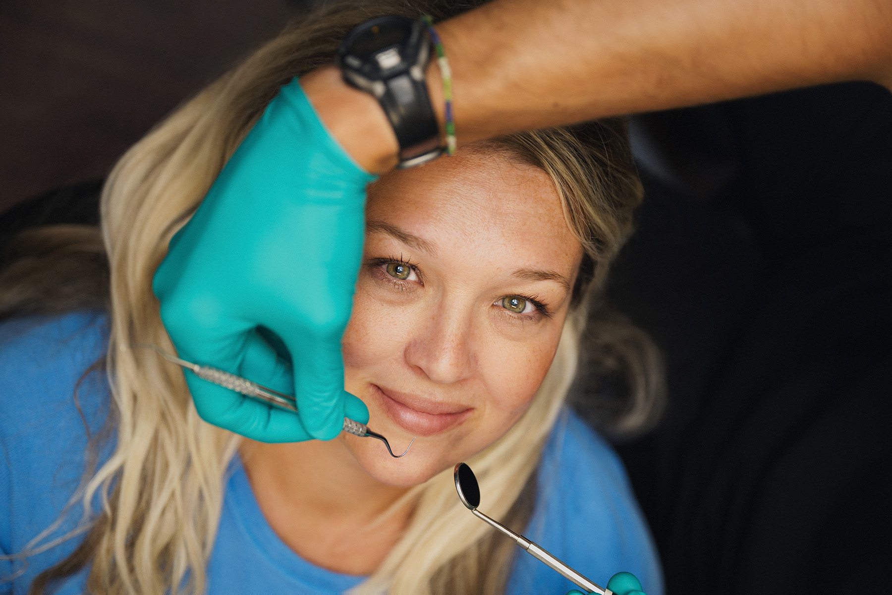 Woman smiling during dental checkup with gloved hands holding dental tools near her face.