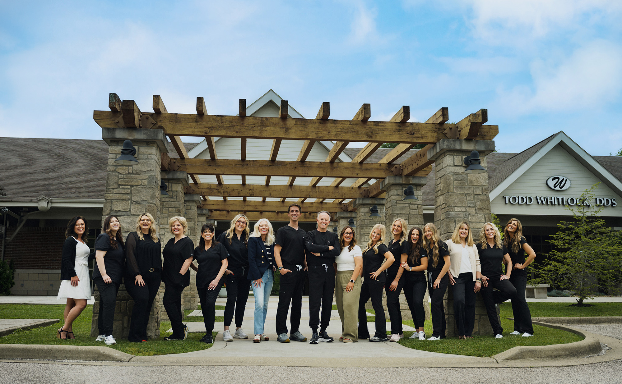 Group of dental office staff posing outside a building with Todd Whitlock DDS sign.