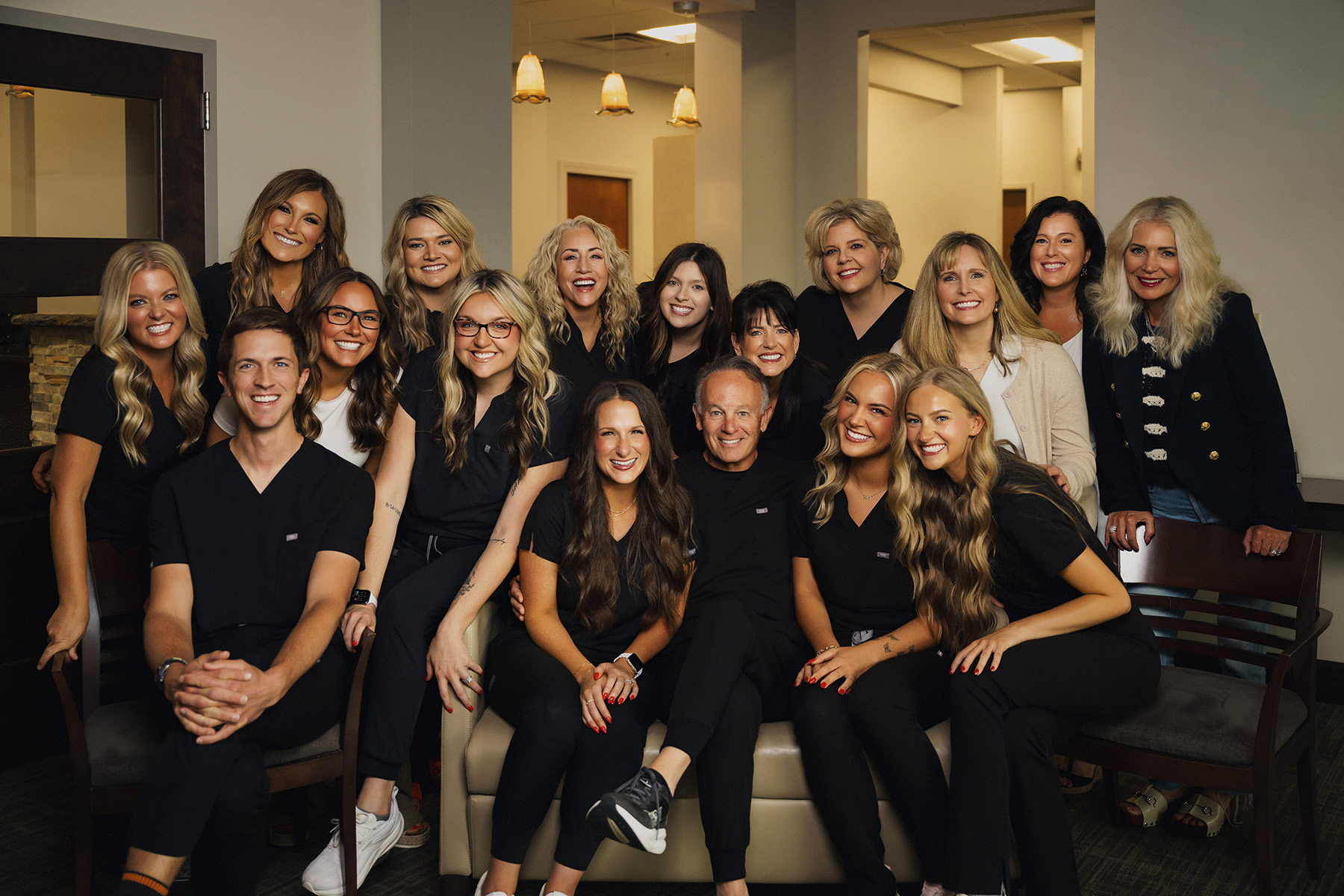 Group portrait of smiling men and women in black outfits posing indoors on and around a couch.