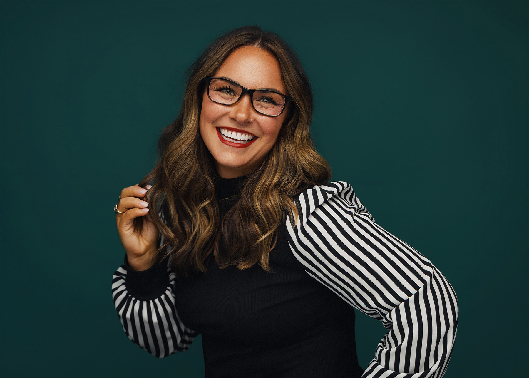 Smiling woman with glasses and striped puff sleeves against a dark green background.