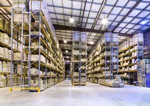 Spacious warehouse interior with high shelves holding stacked boxes and pallets.