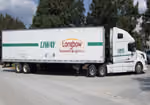 White semi-truck with Longbow Logistics logo parked on gravel near trees under a blue sky.