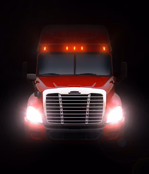 Front view of a red semi truck with headlights and roof marker lights on in the dark.