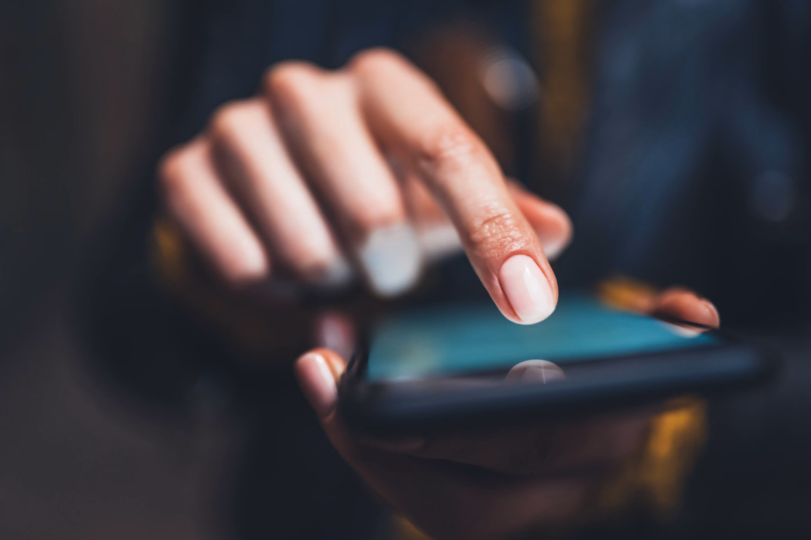 Close-up of a finger tapping a smartphone screen held in one hand with a blurred background.