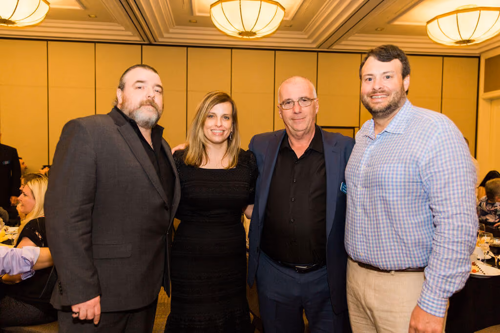 Four adults posing indoors at an event, three men and one woman smiling toward the camera.