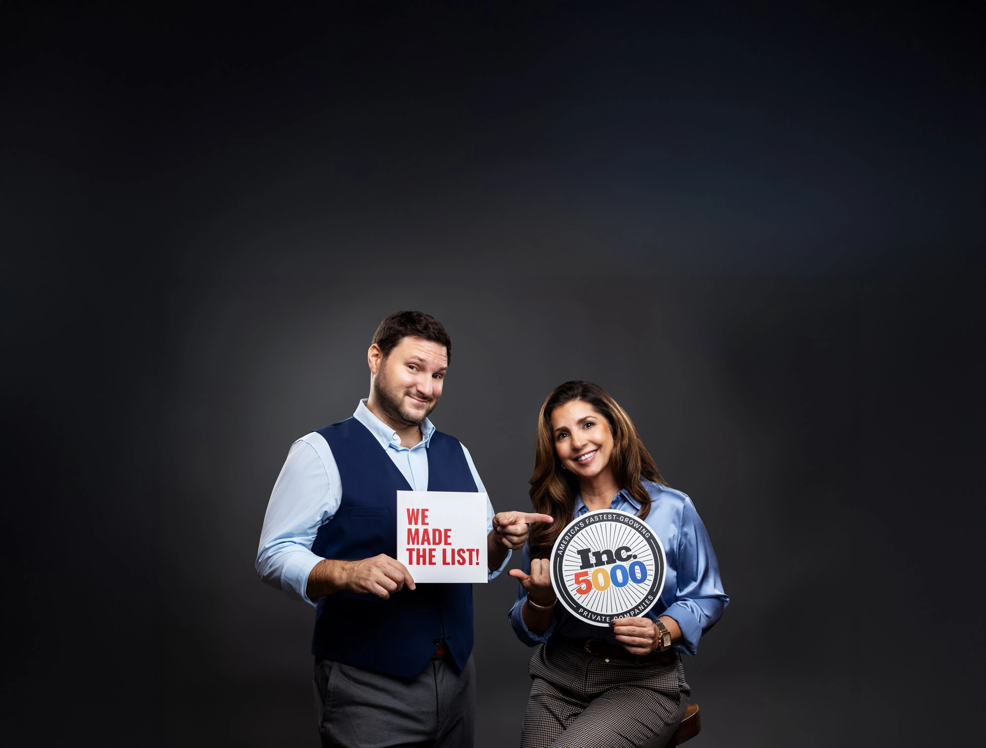 Eddie Laviolette and Jessica Smith, founders of Anntoine Marketing + Design smiling. Eddie is holding a sign saying 'WE MADE THE LIST!' and Jessica is holding an Inc. 5000 award plaque.