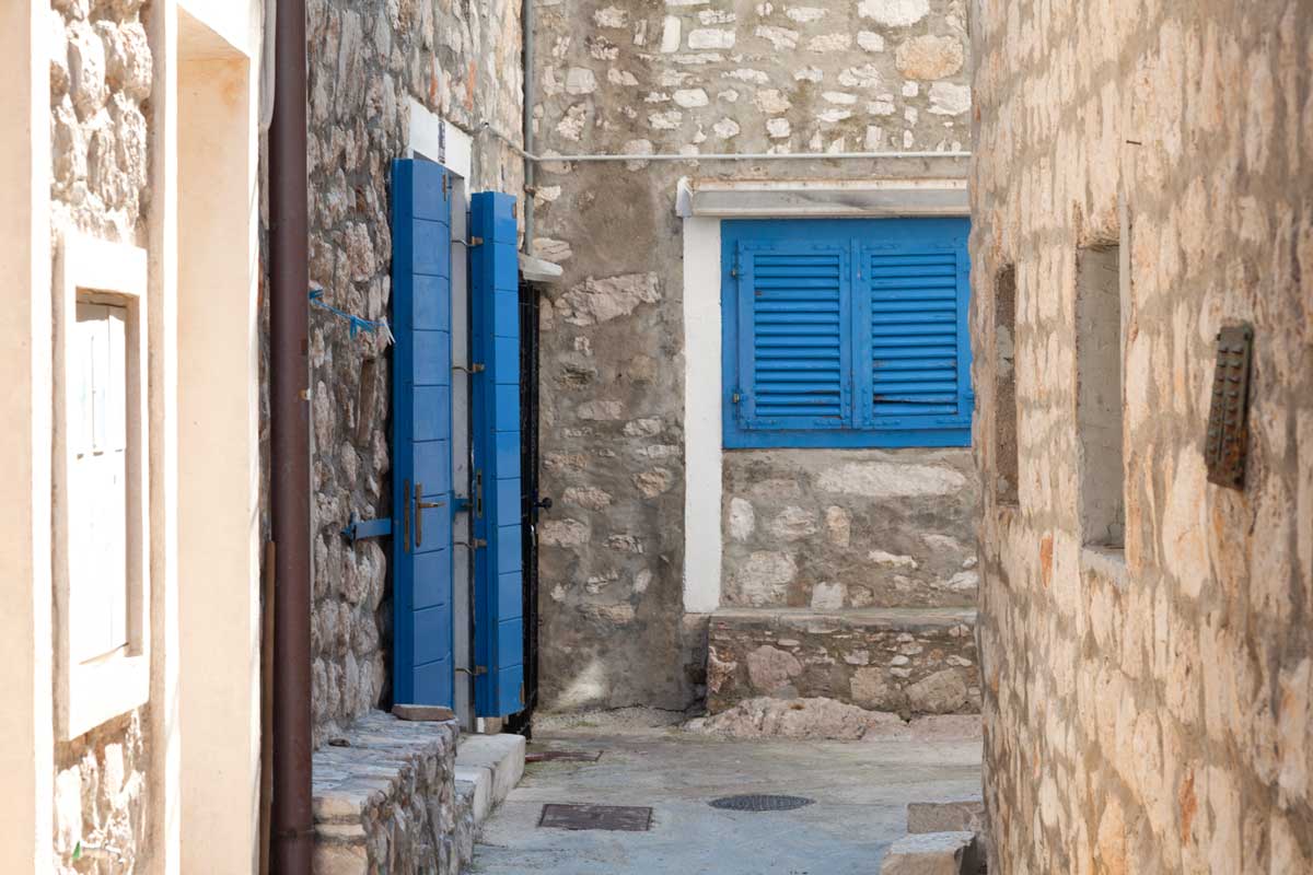 Foto einer engen Gasse in der Altstadt von Tribune mit Steinhäusern mit bleuen Fensterläden