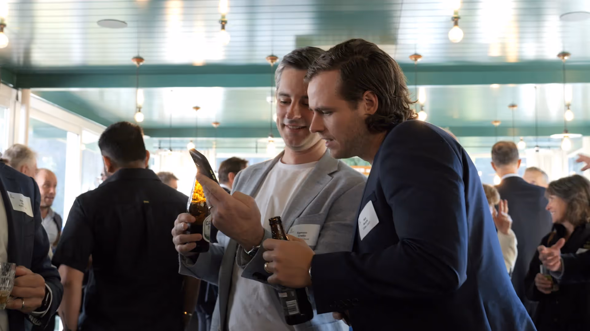 two men holding beer look at phone