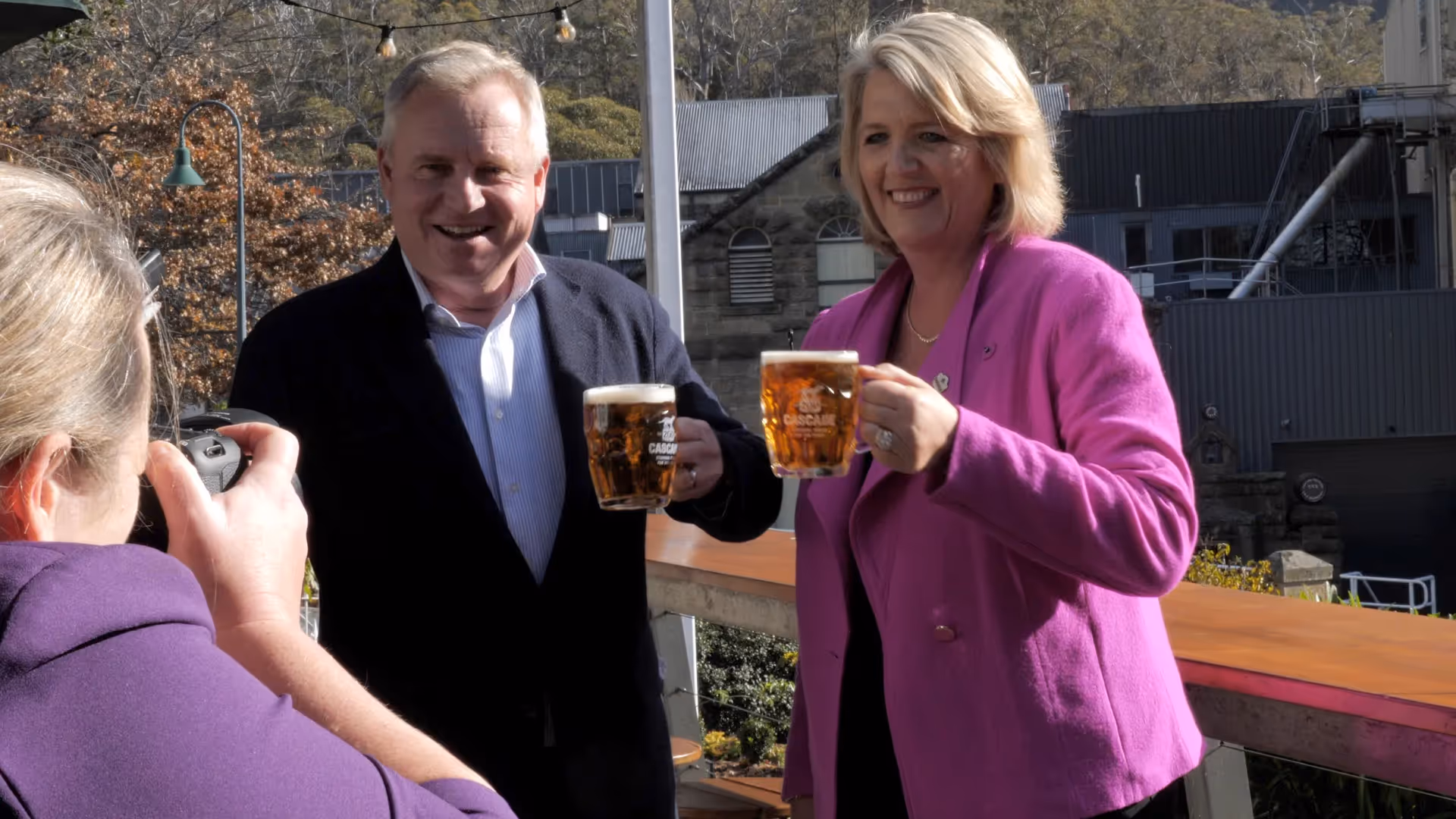 man in blue jacket and woman in pink cheers a cascade beer outside