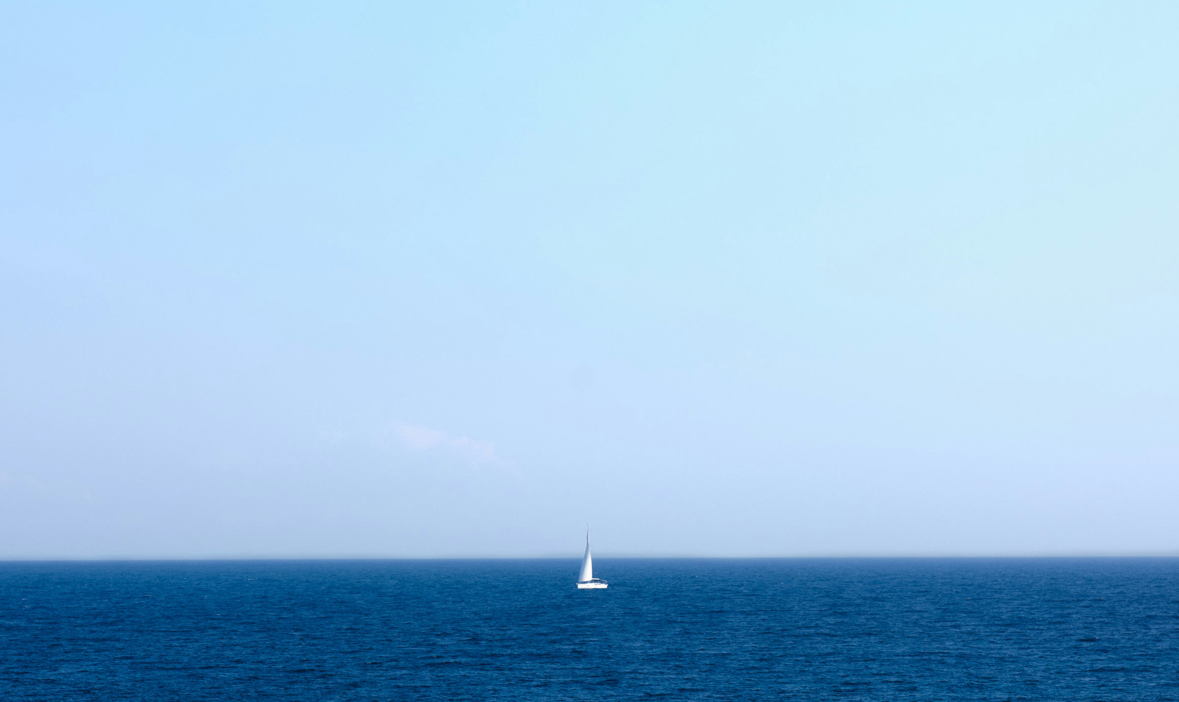Segelschiff mit weißen Segeln, alleine auf dem großen, blauen Meer.
