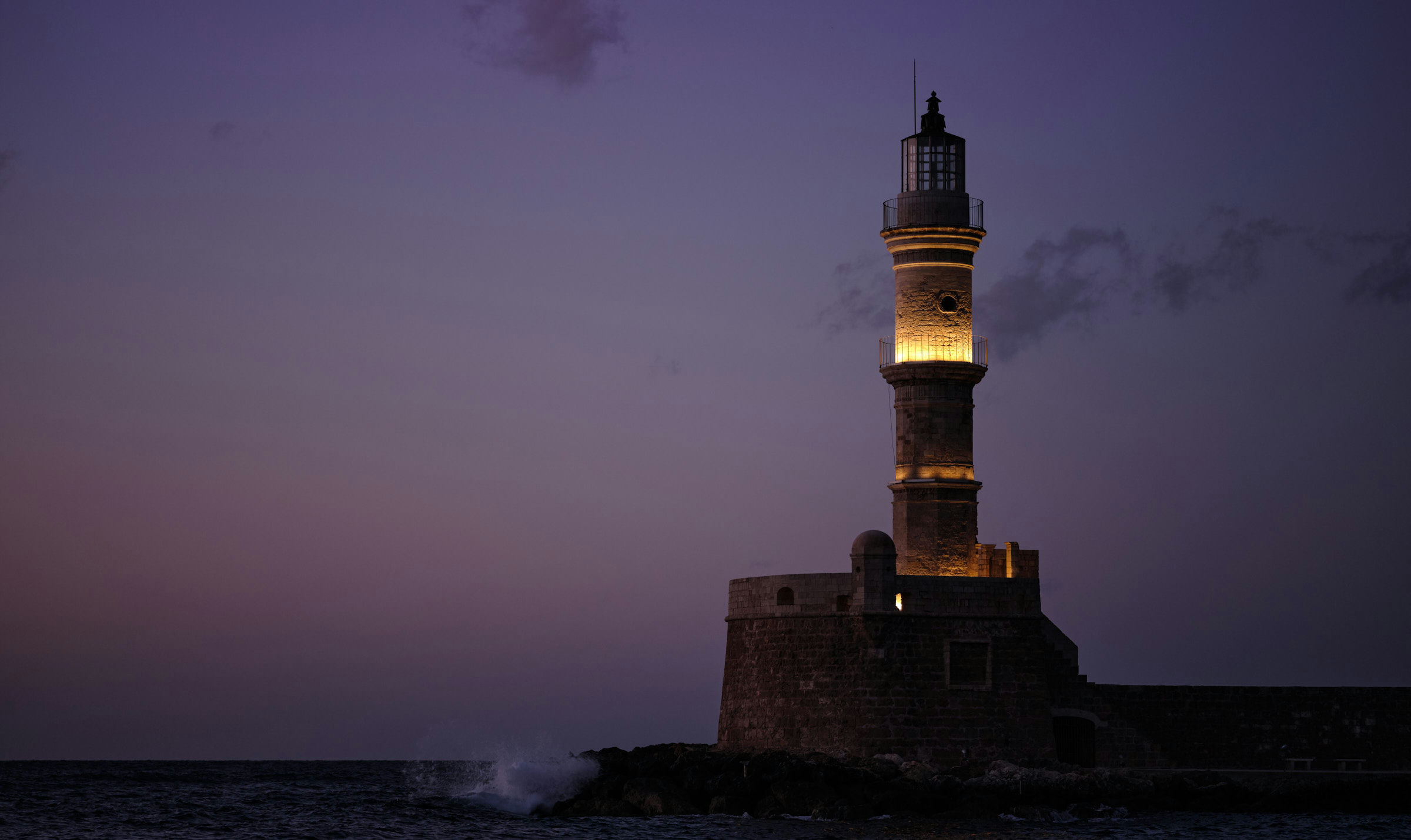 Ein Leuchtturm aus Sandstein erhebt sich in der violetten Dämmerung am Eingang eines Mittelmeerhafens