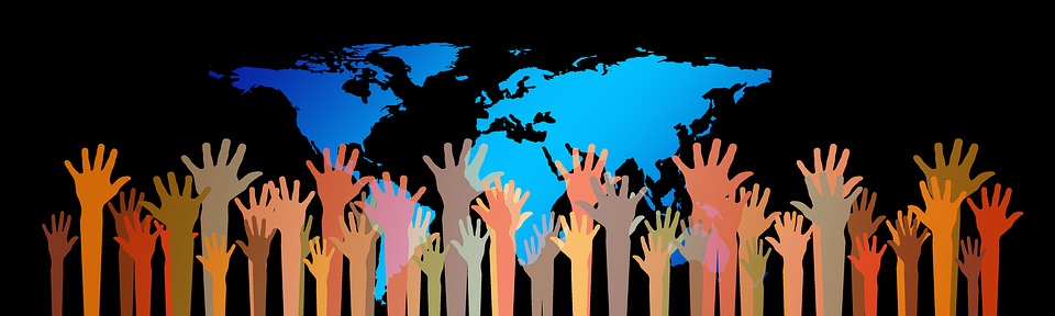 Multiple hands of diverse skin tones raised together in front of a blue world map on a black background.