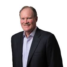 Middle-aged man wearing a dark blazer and light shirt smiling against a white background.