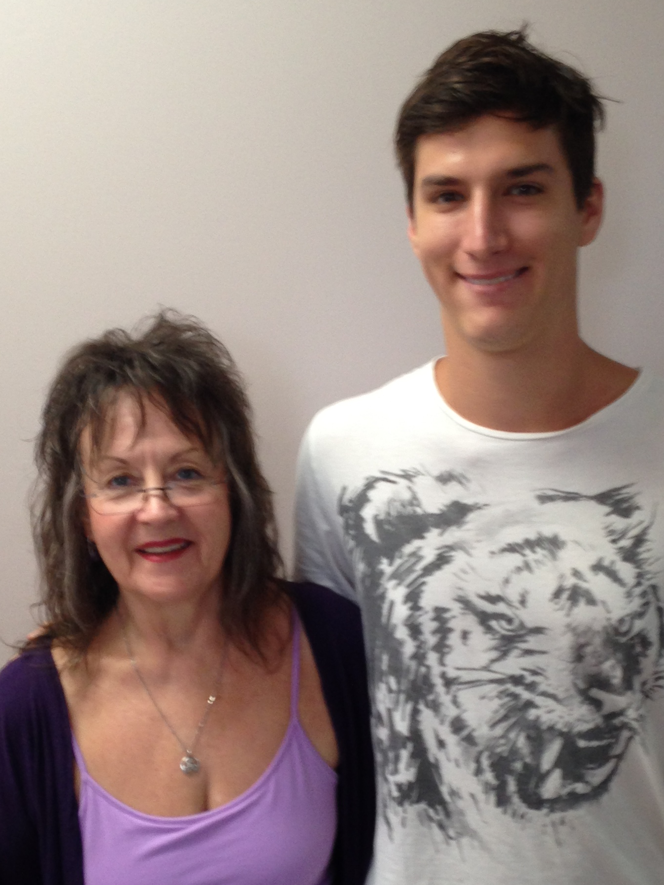 Smiling woman with glasses and purple top standing next to a smiling young man wearing a white t-shirt with a large tiger face print.