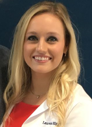 Smiling woman with long blonde hair wearing a white coat over a red top against a blue background.
