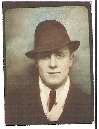 Vintage portrait of a man wearing a dark suit, white shirt, dark tie, and a fedora hat.