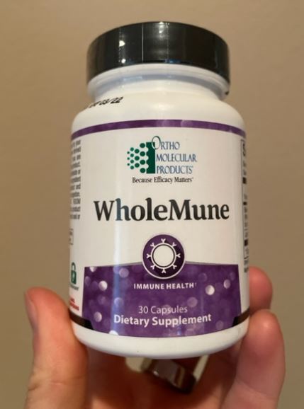 Bottle of WholeMune dietary supplement with immune health support, containing 30 capsules, held in a hand.