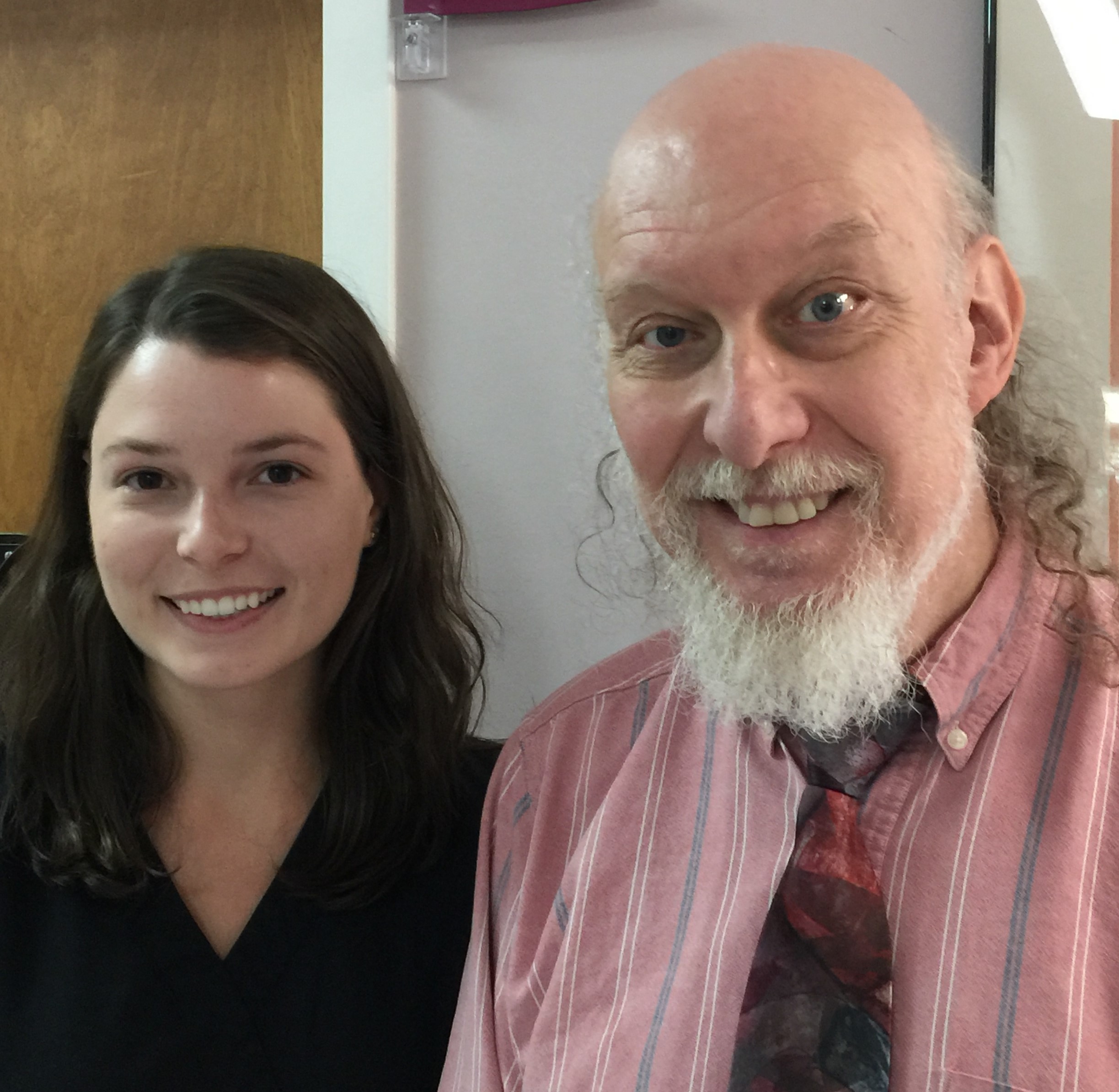 Smiling middle-aged man with a white beard and a bald head standing next to a smiling young woman with dark hair.