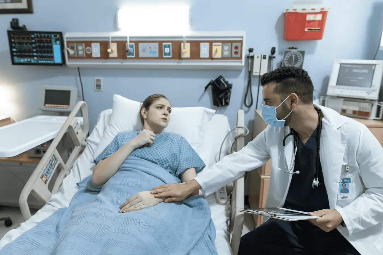 A doctor converses with a patient who is resting in a hospital bed, providing care and support during their recovery.