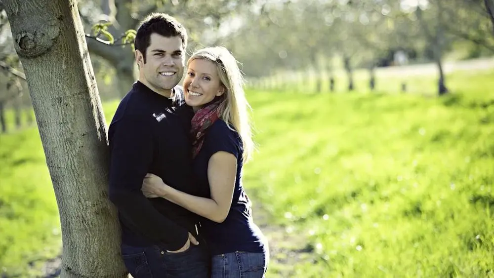 Couple Phil and Alex posing leaning against a tree