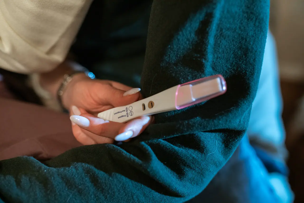 A close up of a hand with long fingernails holding a positive pregnancy test.