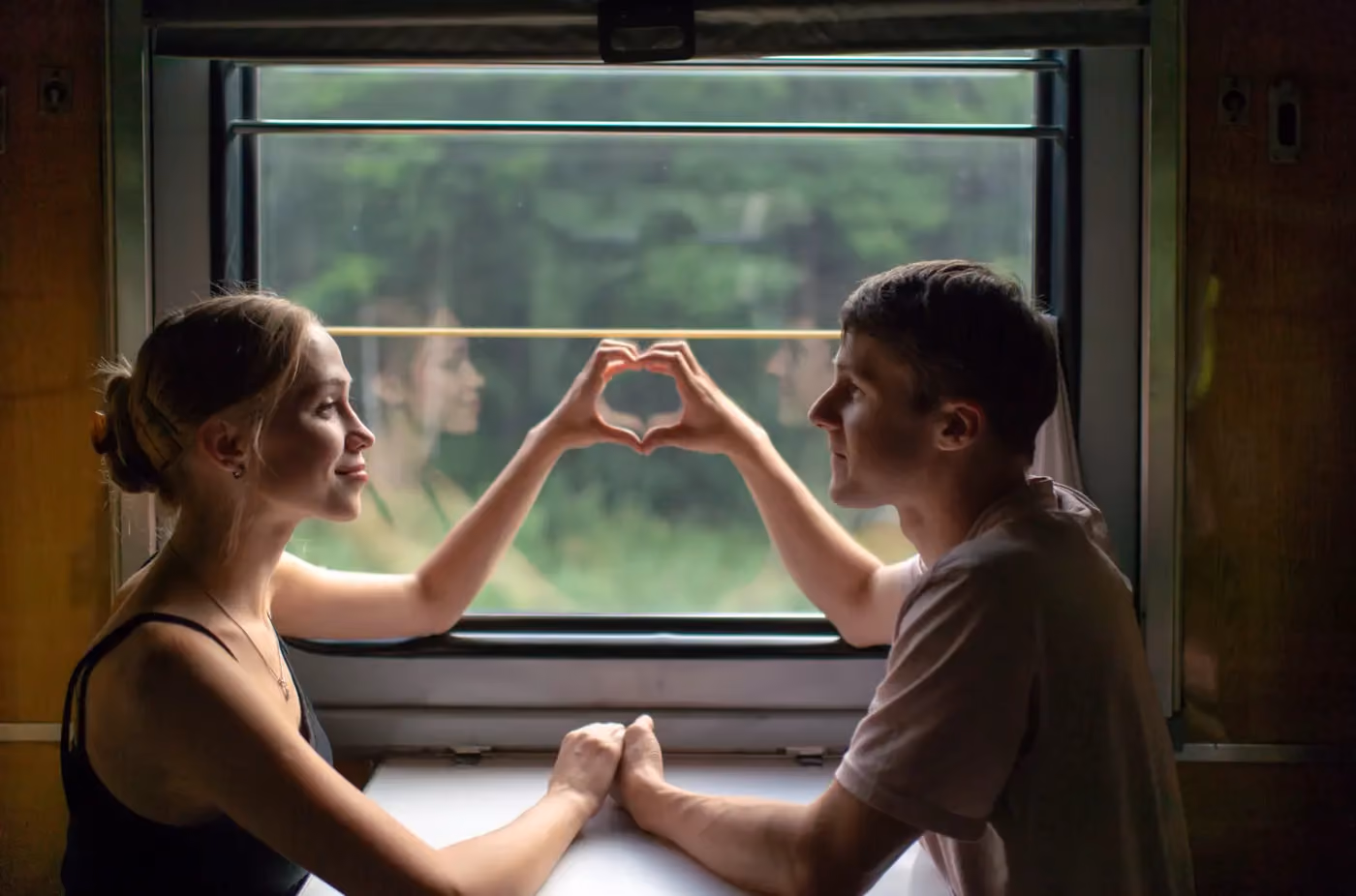 lovers holding hands across a table in front of a window epresenting the inexplicable pull of a past life romantic connection across lifetimes.