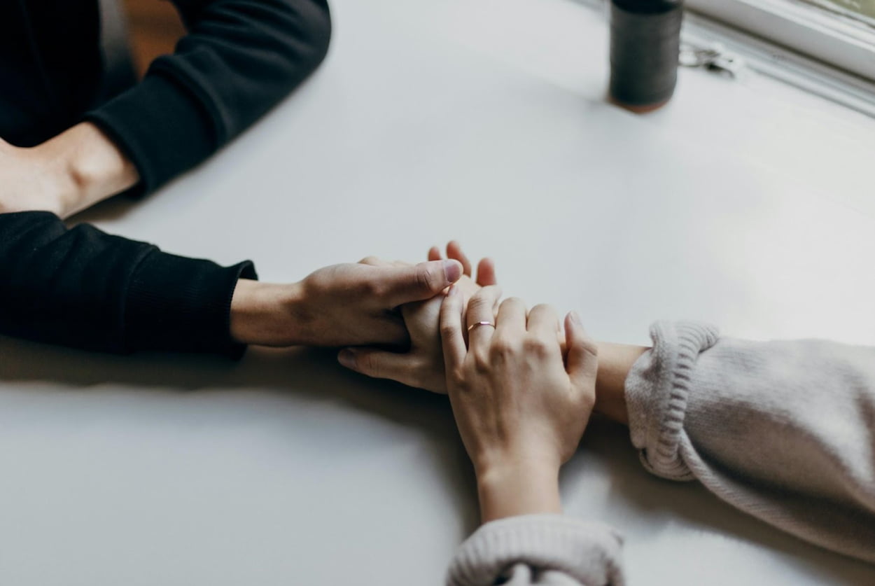 Two people holding hands across a table, symbolizing connection and intimacy.  