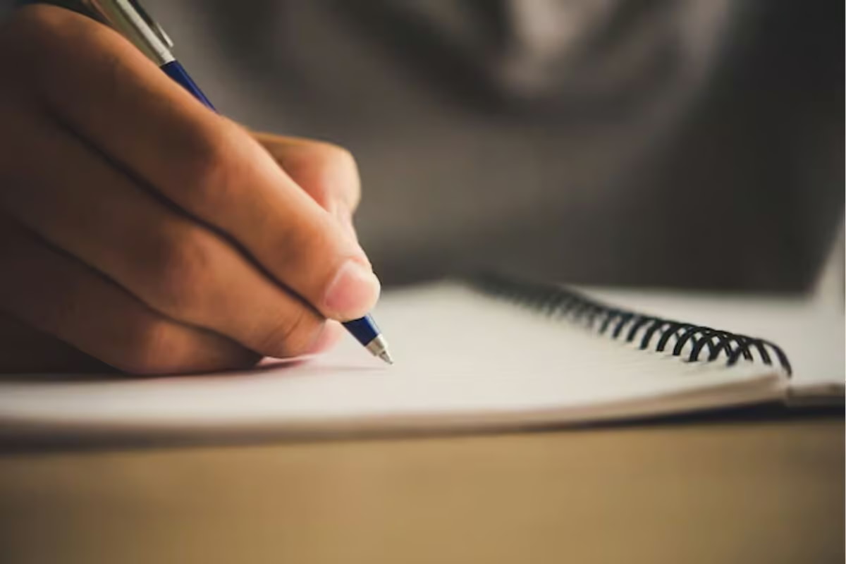 A person writing in a notebook with a pen, focused on their task in a well-lit environment. 