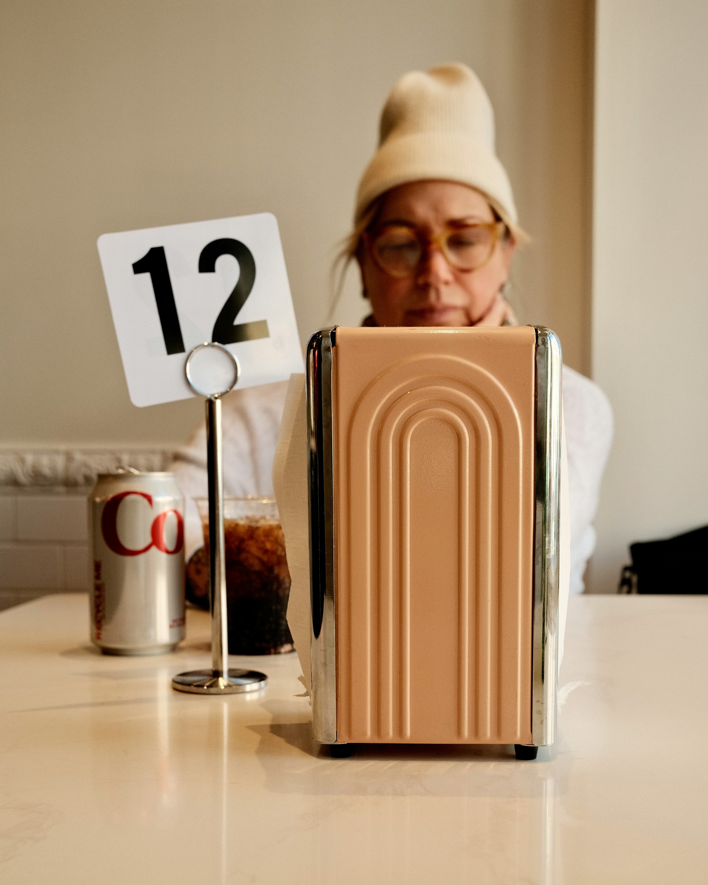 A woman sitting at a table with a can of Coke and a napkin holder.