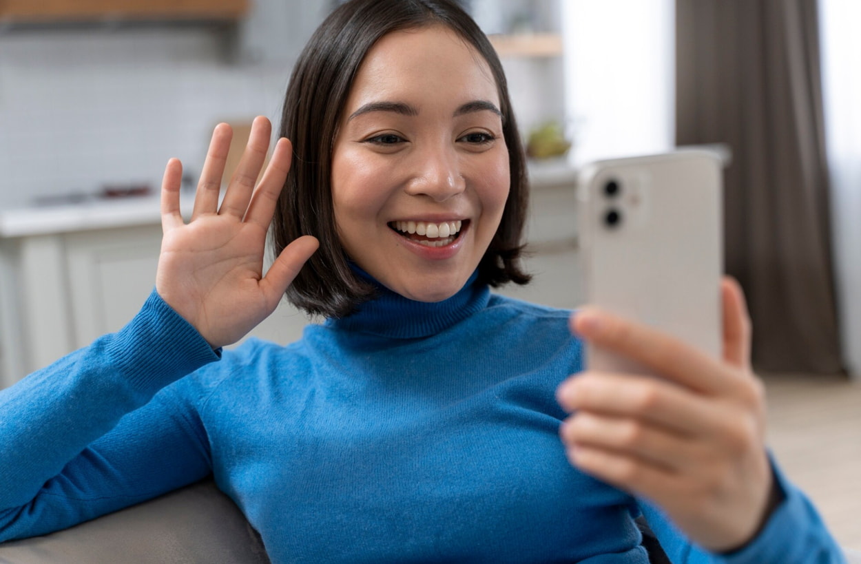 A woman smiles while holding her phone up, capturing a joyful moment. 