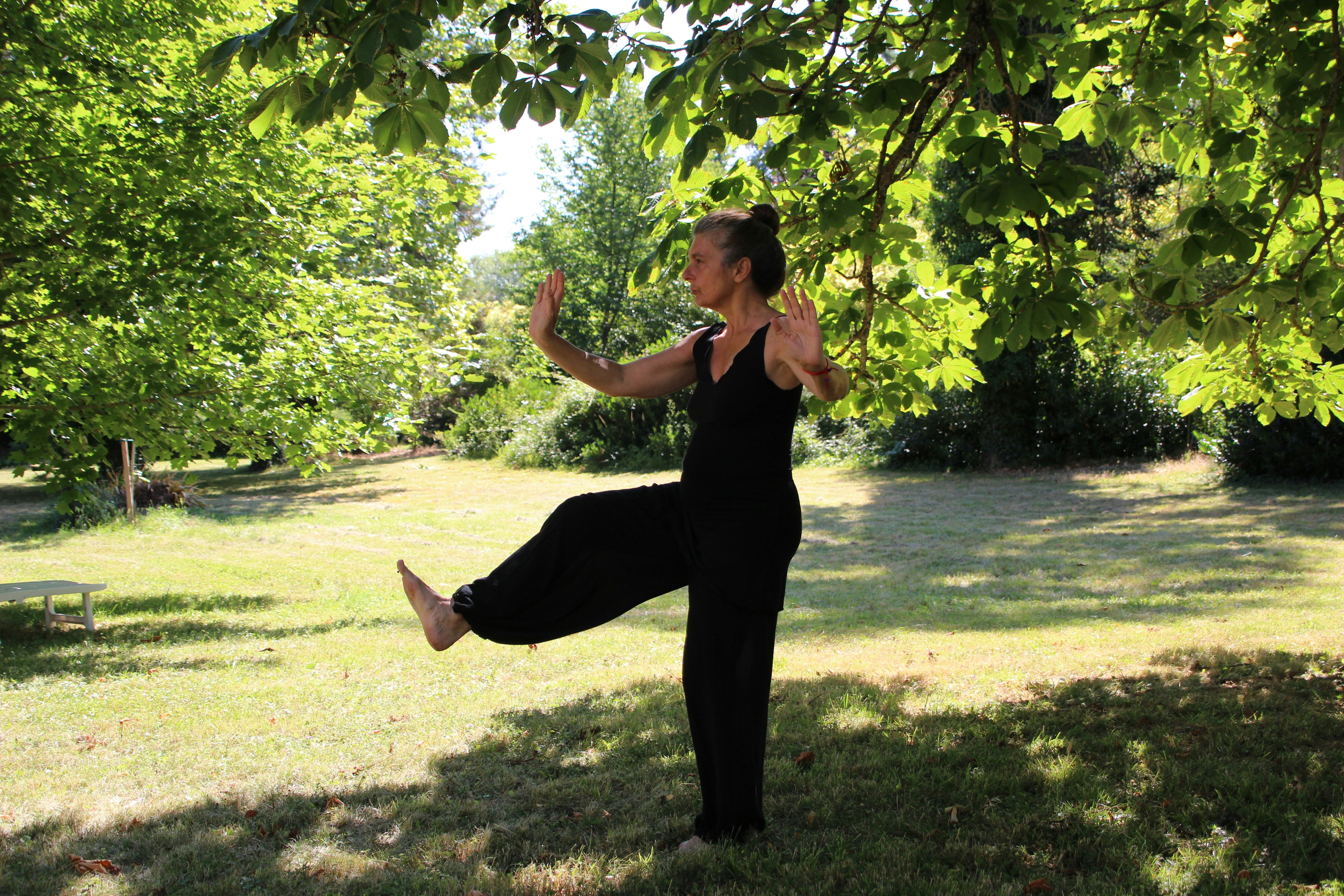 A woman in a black sleeveless one-piece standing under a tree during the daytime