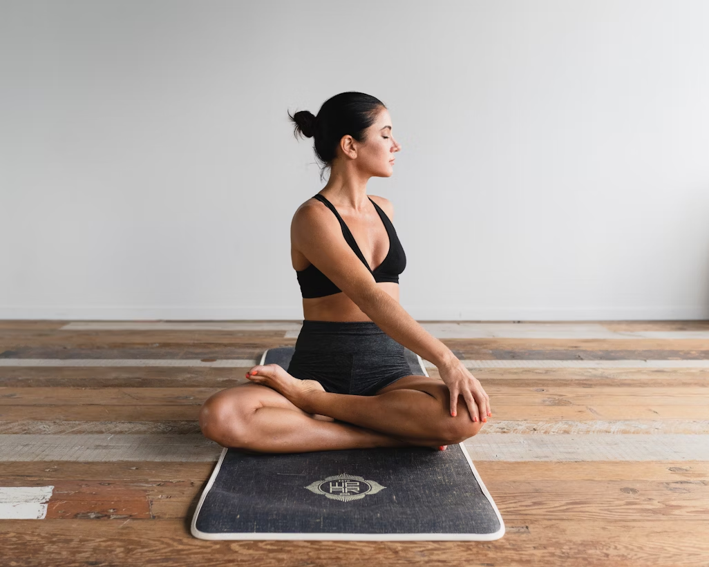A woman doing a yoga stretch on a yoga mat on wood.