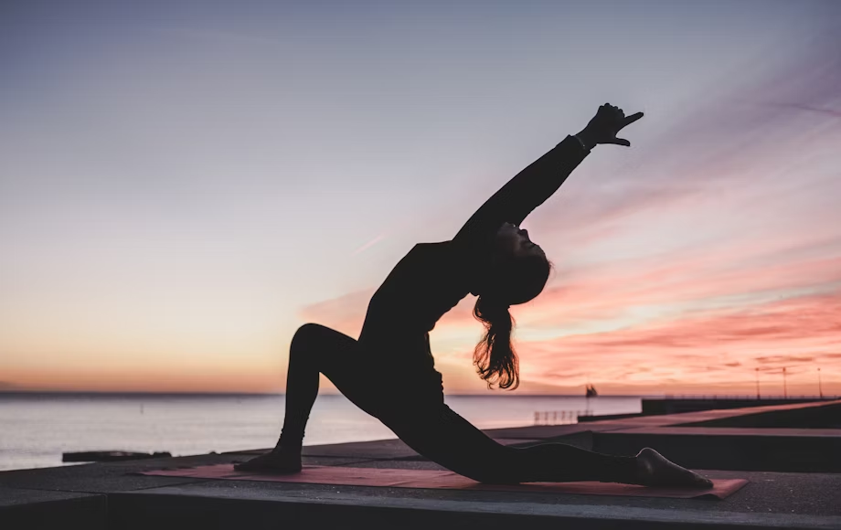 A silhouette photograph of a woman doing yoga by a large body of water