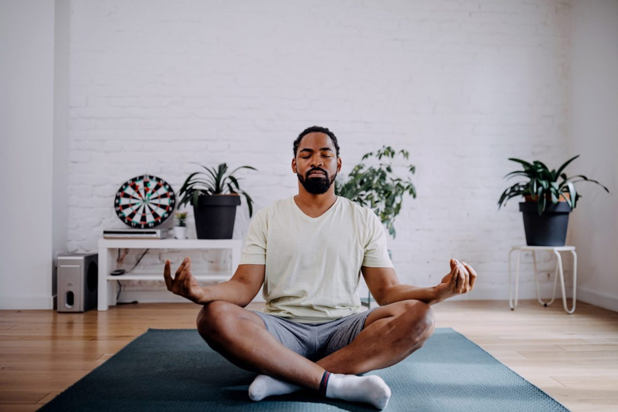 A man sitting cross-legged in a yoga pose, eyes closed, practicing meditation in a serene environment. 