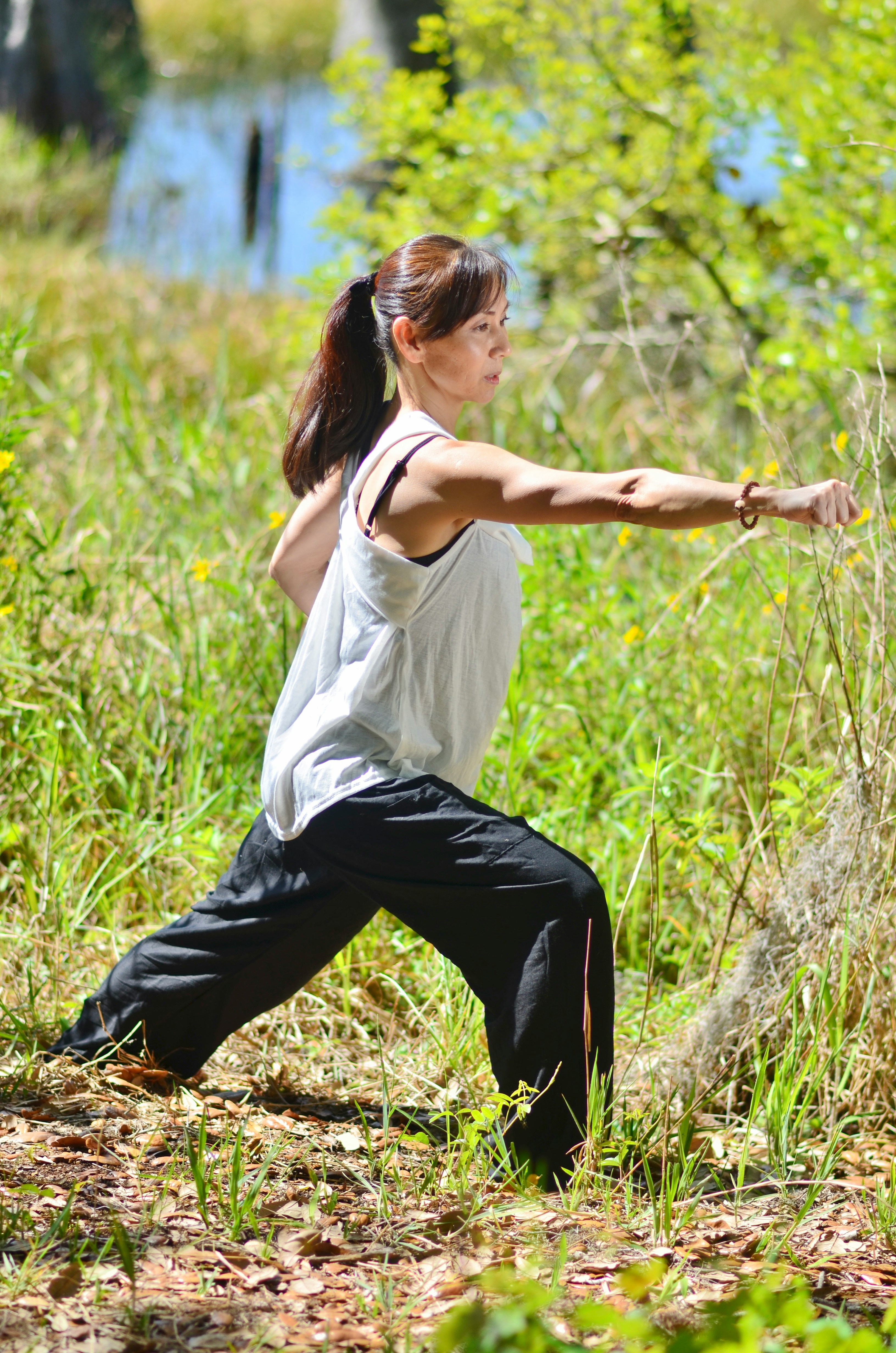 A woman in black pants and a white tank top stretching.