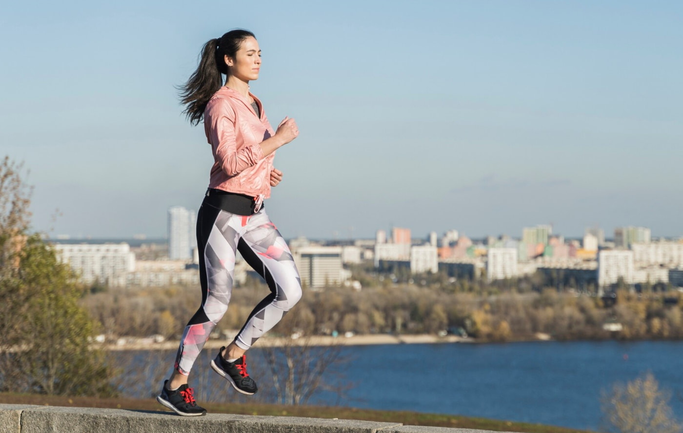 A woman in a pink jacket and leggings runs along a vertical wall, showcasing her agility and athleticism. 