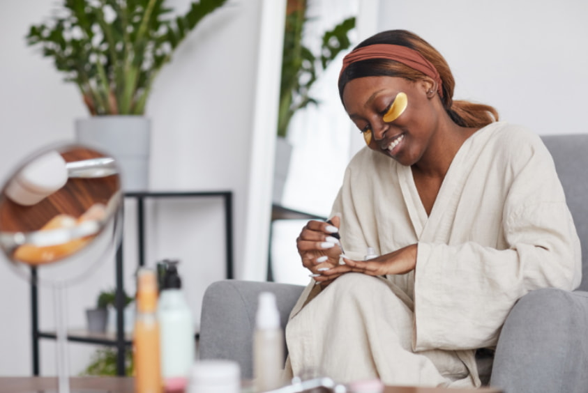 A woman in a robe sits on a couch, looking polished with her makeup done, exuding a relaxed yet elegant vibe. 