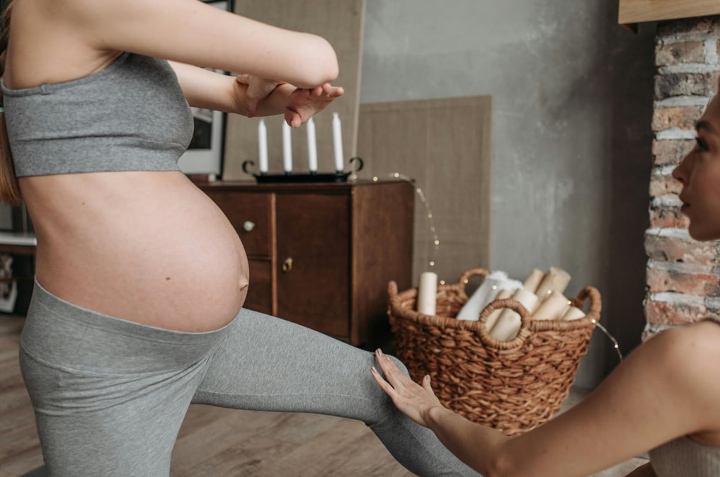 A pregnant woman practices yoga alongside another woman in a serene indoor setting. 