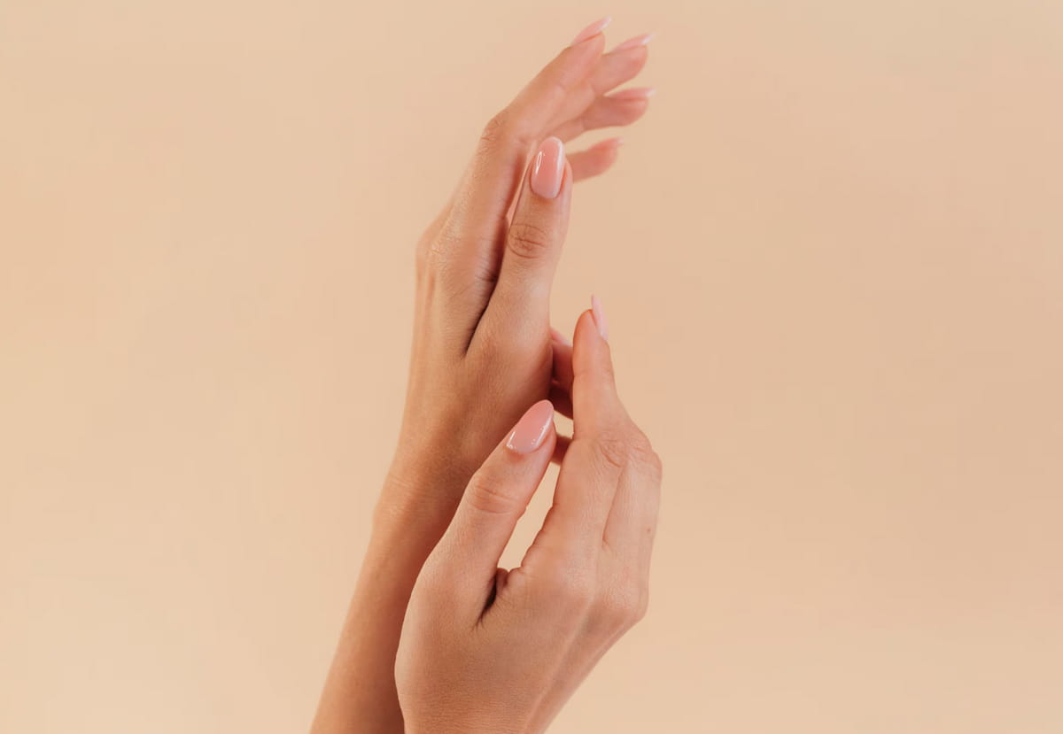 A close-up of a woman's hands with elegantly manicured pink nails resting on a soft surface.  