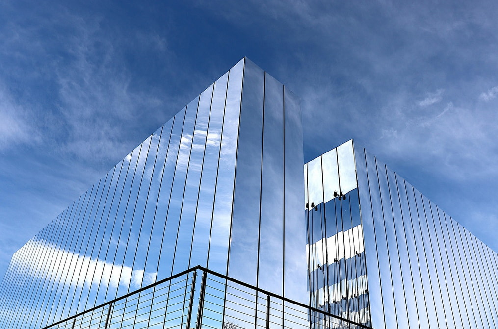 A sleek building with a glass exterior reflecting a bright blue sky and scattered clouds.